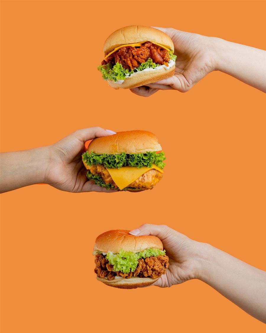 Trois burgers tenus à la main sur fond orange